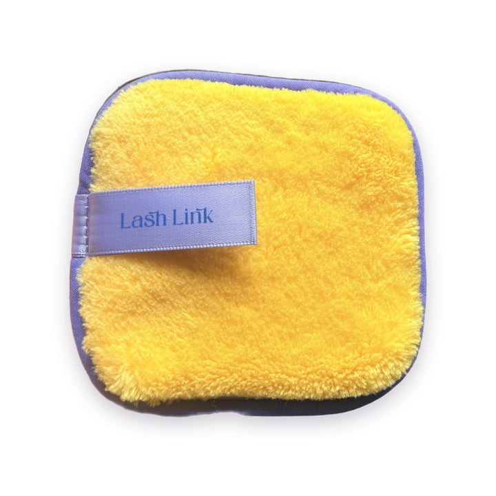 Lash Link Cleansing Sponge, a plush yellow microfibre makeup remover pad with lilac edging and a lilac satin Lash Link tab, on white
