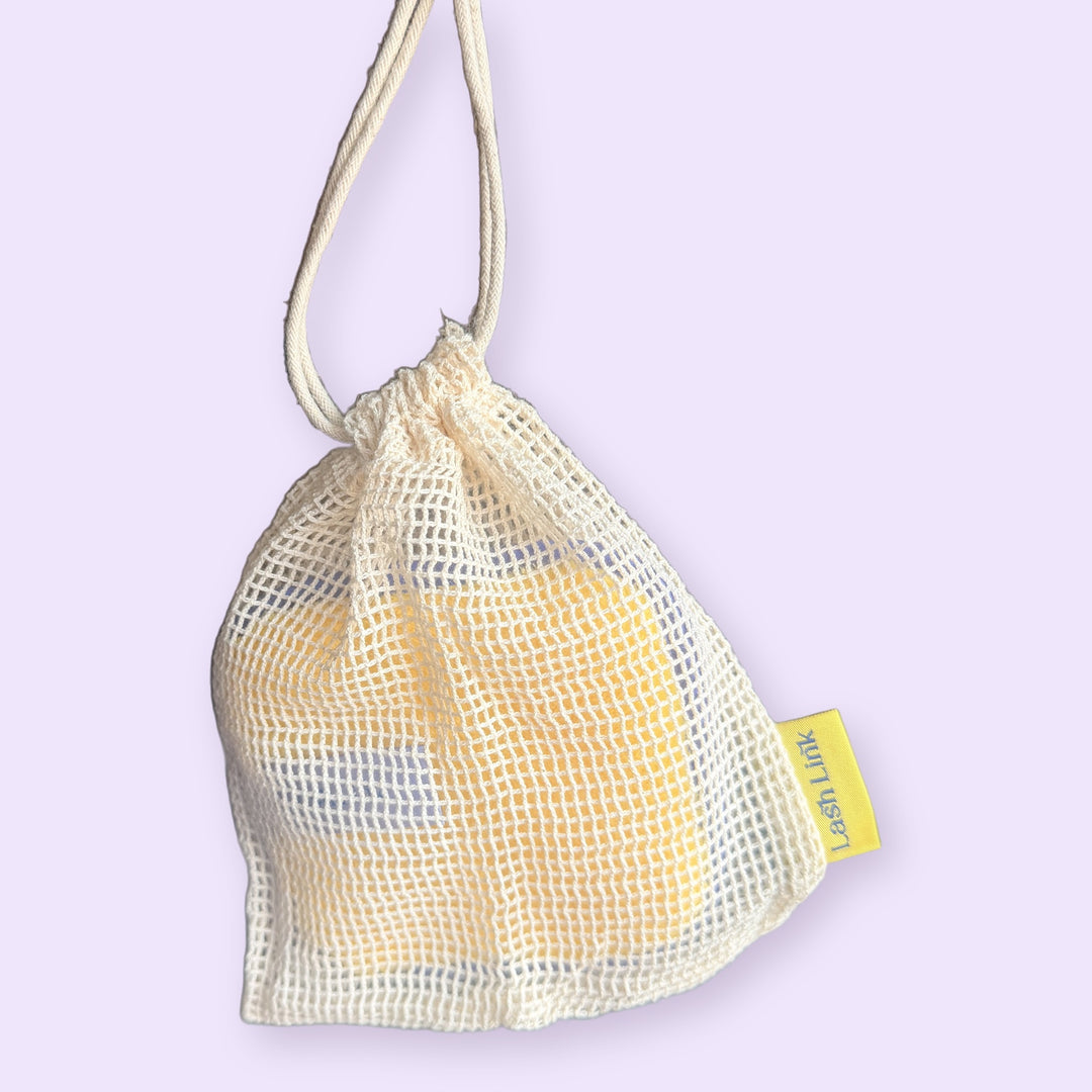 Cotton mesh drawstring bag hanging by its string with the Lash Link Cleansing Sponge inside, so it can dry in the shower