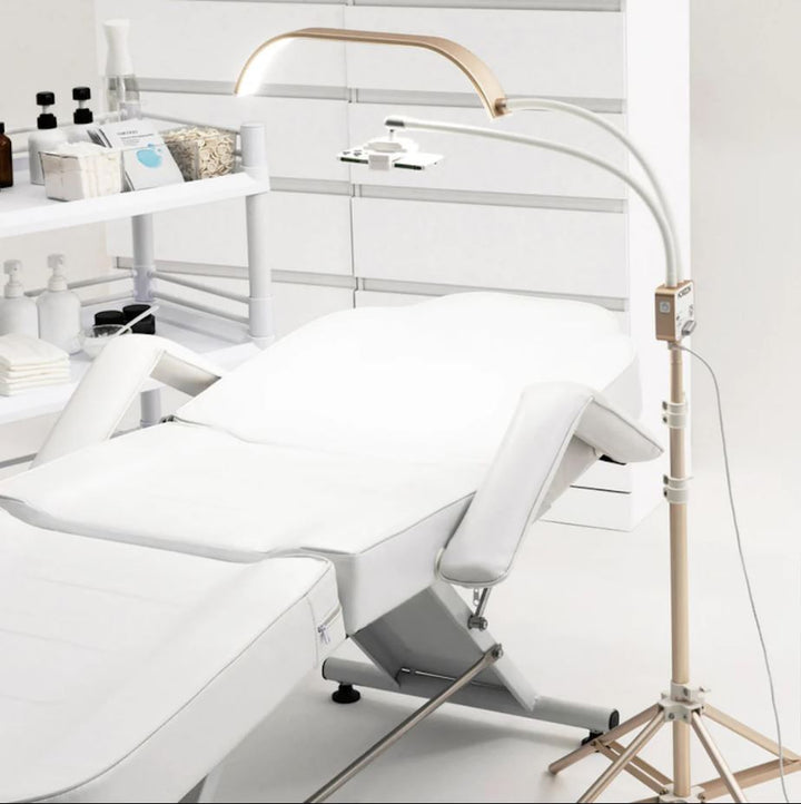 A white bed with the Lash Tribe GLAMCOR Horizon Pro Kit | Light for Lashing in the middle, providing lighting for a lash artist.