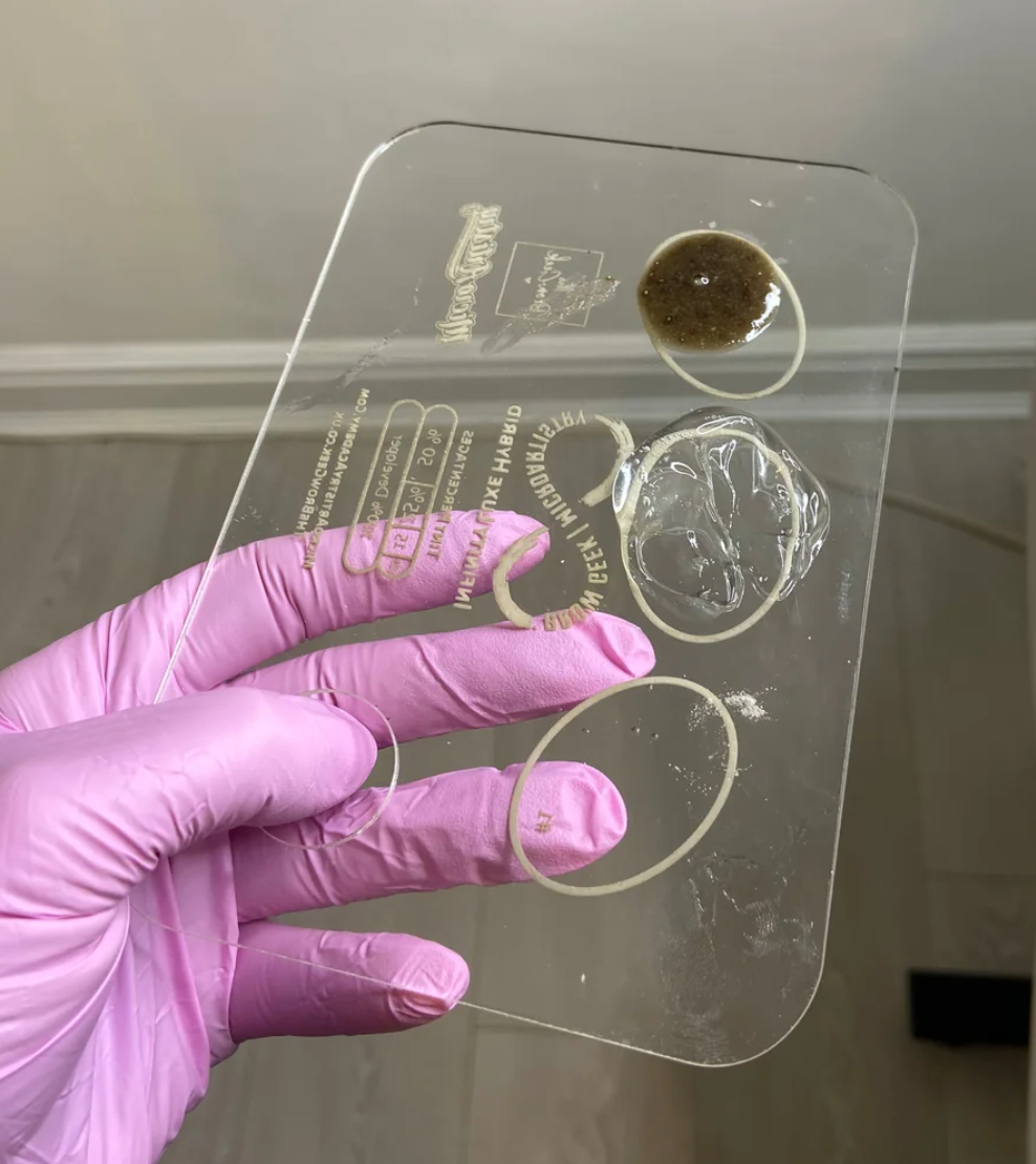 a person holding up a clear plastic INFINITY LIFT &amp; TINT PALETTE by Lash Tribe, which is used for eyebrow and lash lifting.