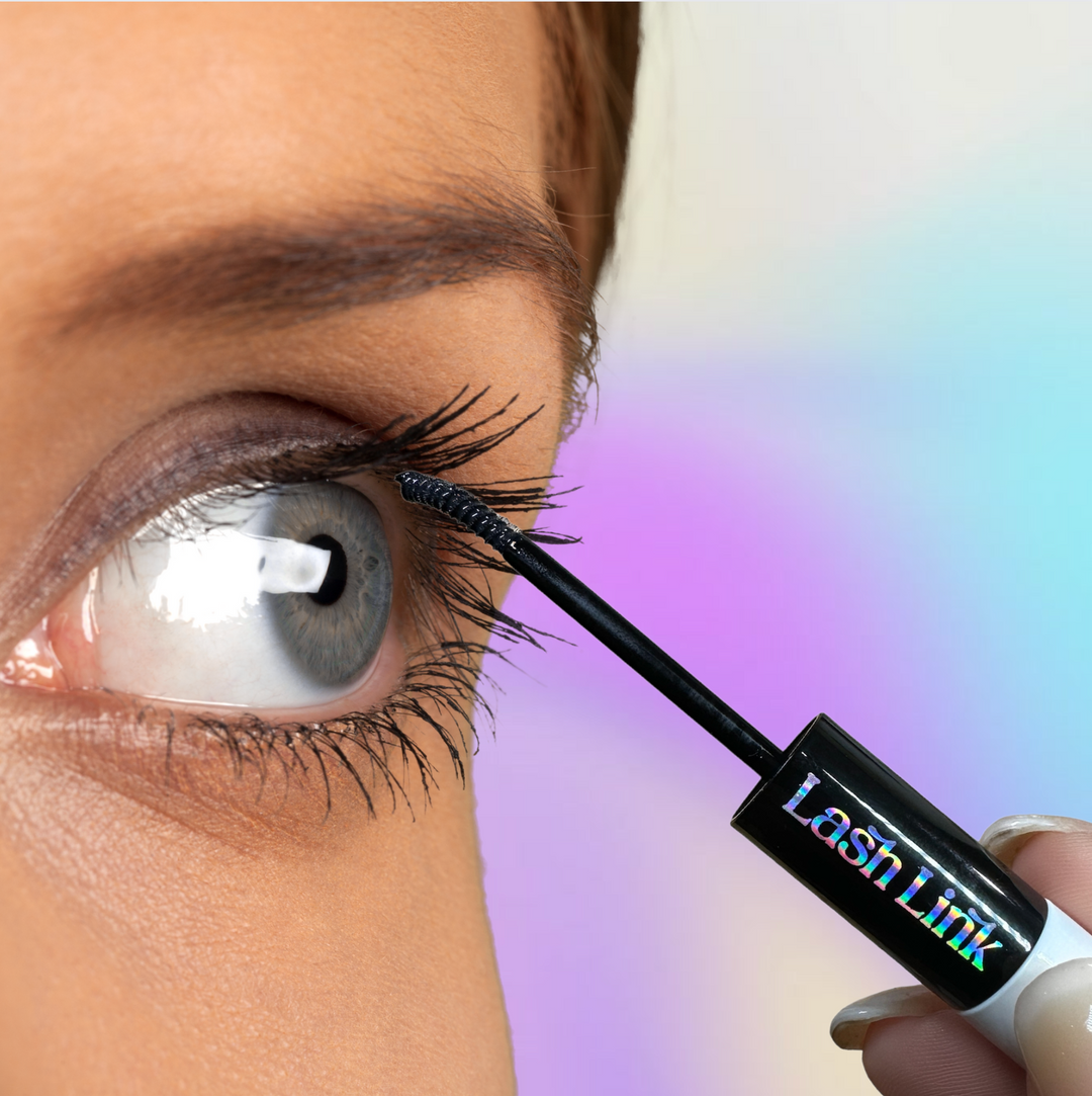 Close-up of a person expertly using the Lash Link Applicator | Lash Segment Tweezer by Lash Link for flawless mascara on upper eyelashes. A soft pastel gradient in the background enhances the scene&