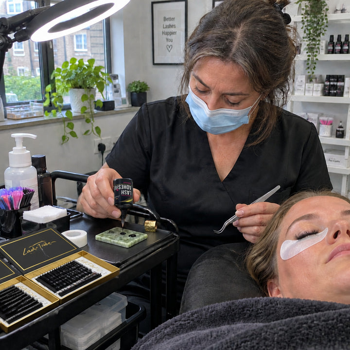 Lash artist adding a drop of Lash Tribe Rapid Black lash glue to a jade tile during an eyelash extension appointment