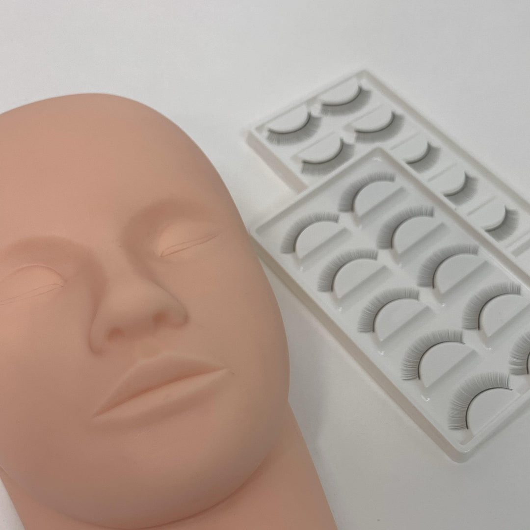 A Lash Tribe Mannequin Practice Head is placed next to two trays of practice lashes, each containing several pairs of false eyelashes.