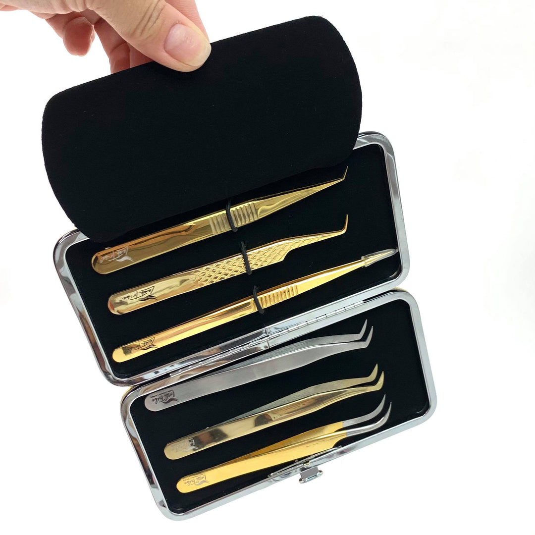 A hand holds an open Gold Magnetic Tweezer Case by Lash Tribe, featuring six precision tweezers with gold and silver finishes, neatly organized in foam slots.