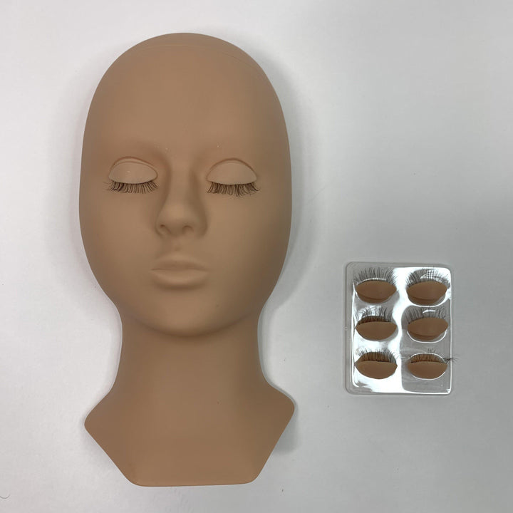 A Lash Tribe Mannequin Practice Head with interchangeable eyelids and closed eyes, complete with applied false eyelashes, is positioned next to a set of false lashes in a transparent case.