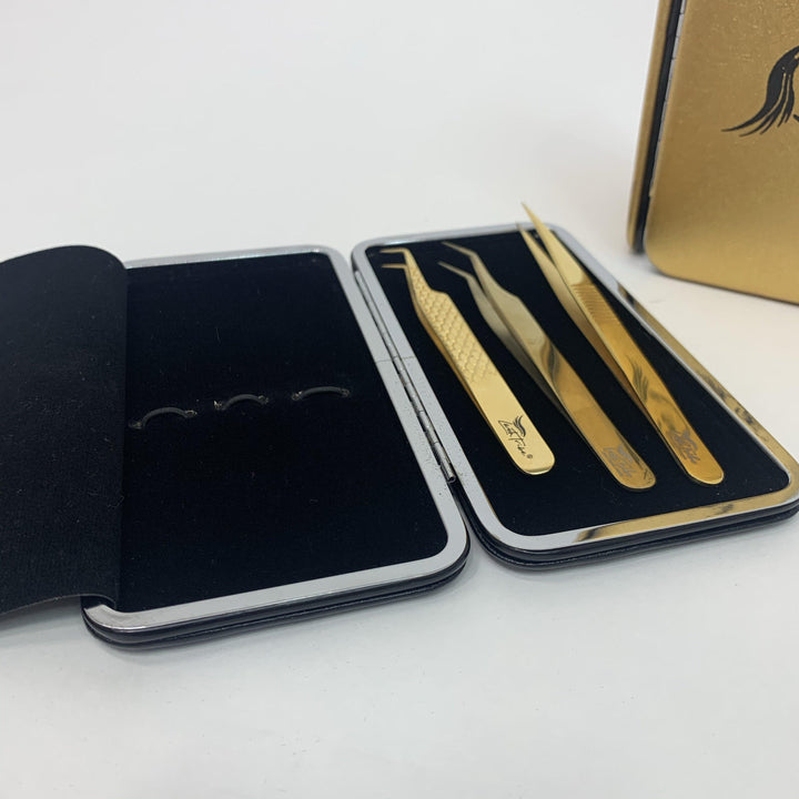A set of three gold-colored tweezers in a stylish black and gold magnetic case with a butterfly logo, brought to you by Lash Tribe&